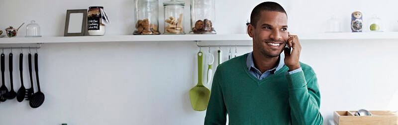 smiling man in his kitchen talking on the phone in a green jumper