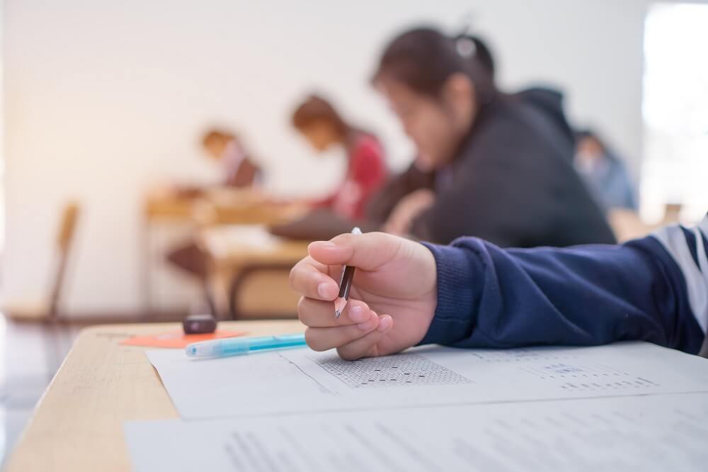 exam room filled with students holding pencils