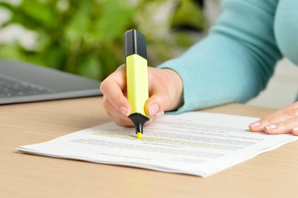 woman in a blue top highlighting a document with a yellow highlighter