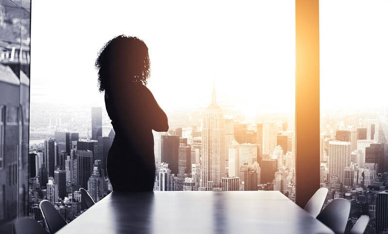 female lawyer standing in a boardroom overlooking a city skyline with arms crossed in silhouette 